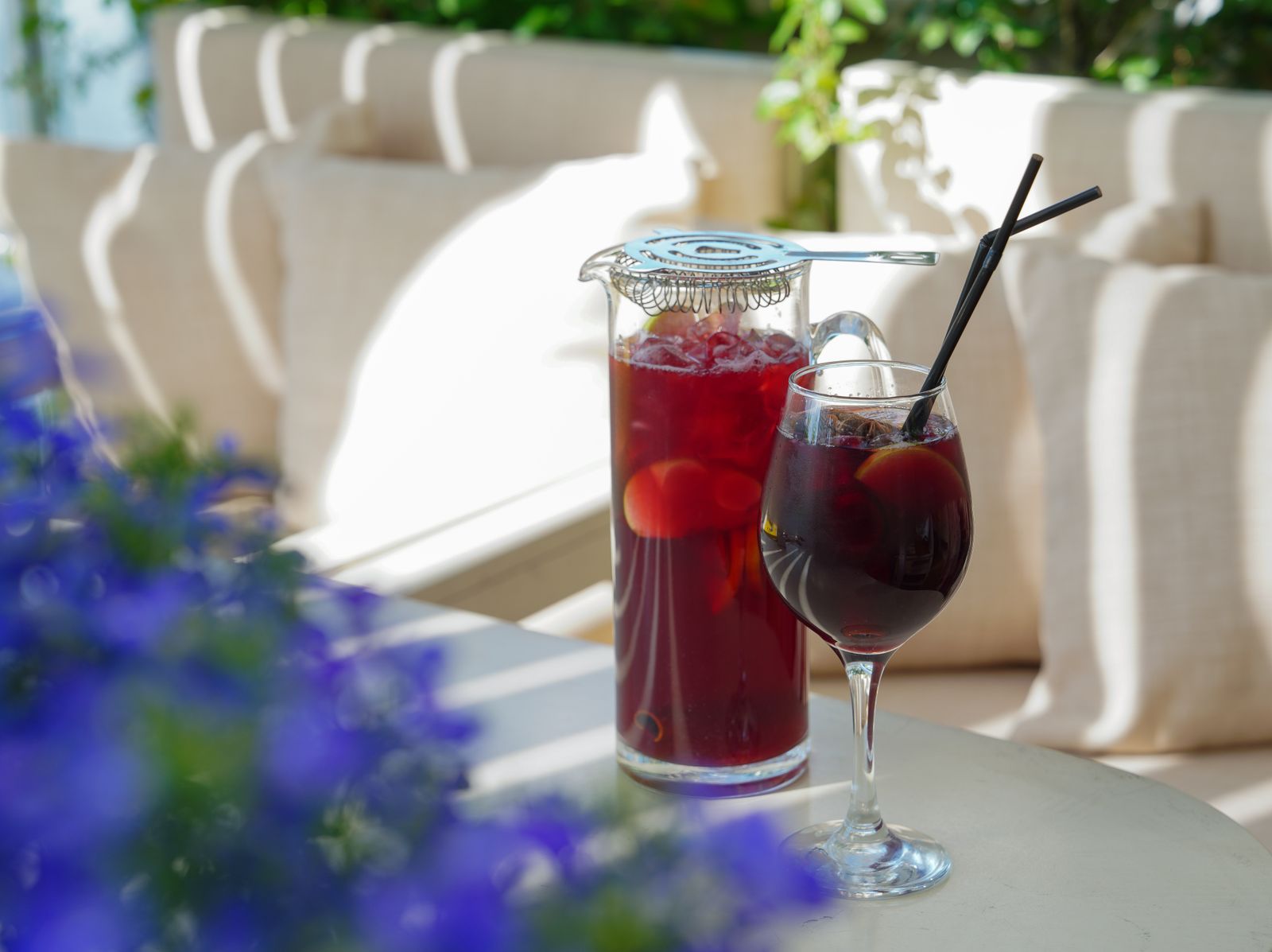 Krug mit fruchtiger Bowle und Trinkhalmen auf einem sonnigen Gartentisch