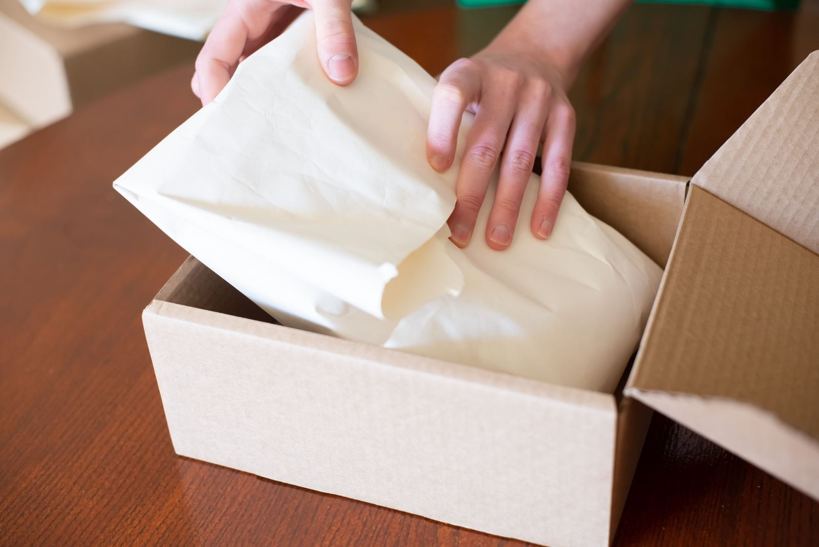 Hände verpacken eine Bestellung sorgfältig in einen Versandkarton