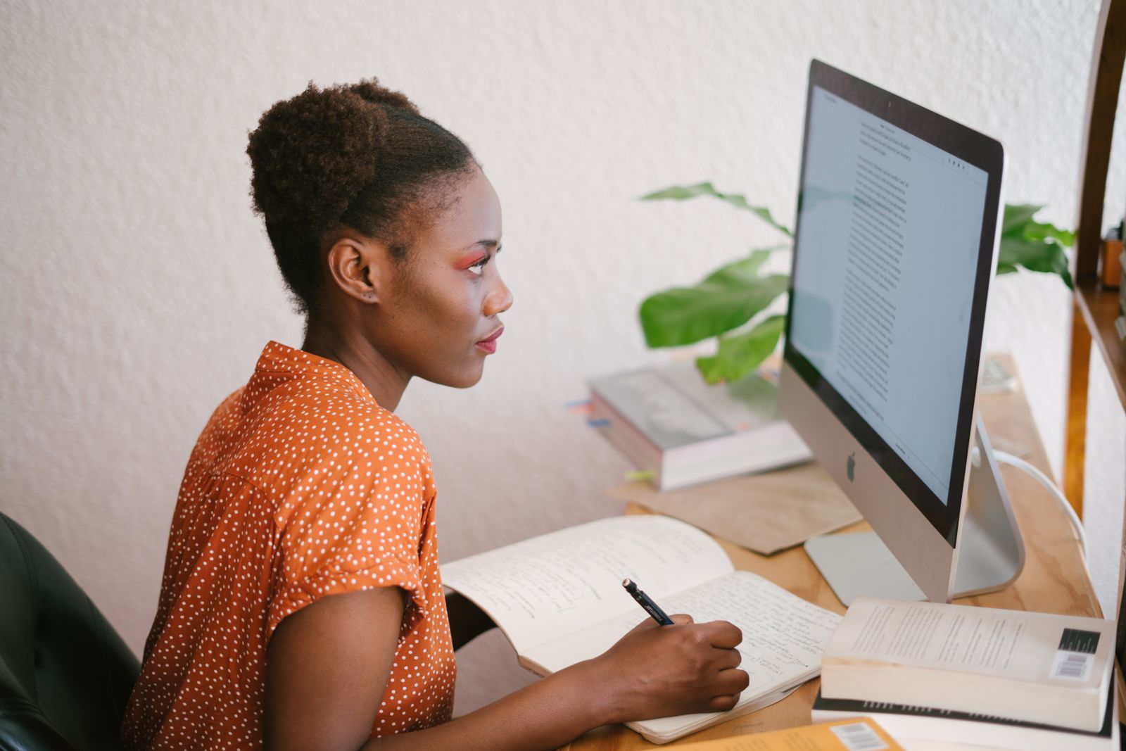 Junge Frau arbeitet konzentriert am Laptop an ihrem Schreibtisch mit Büchern und Notizen