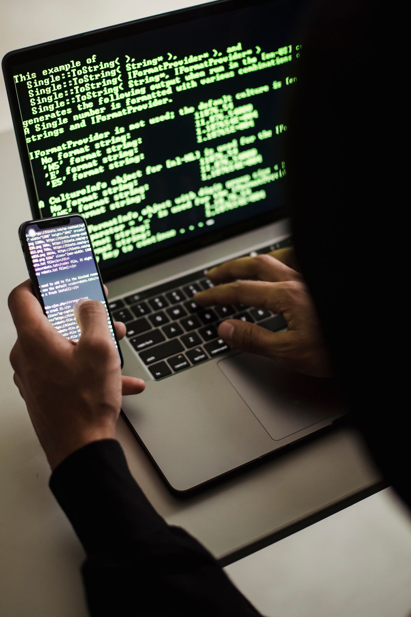 Person arbeitet am Laptop und prüft Smartphone-Benachrichtigung zur Kontosicherheit
