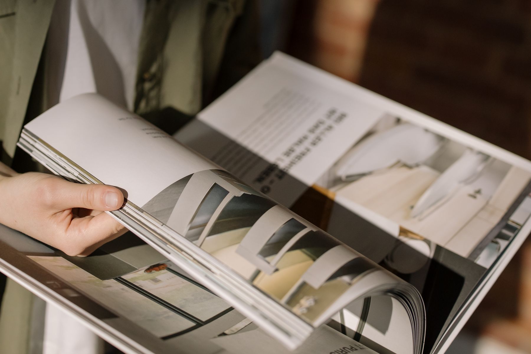 Hand blättert durch die Innenseiten eines aufgeschlagenen Architektur- und Design-Magazins