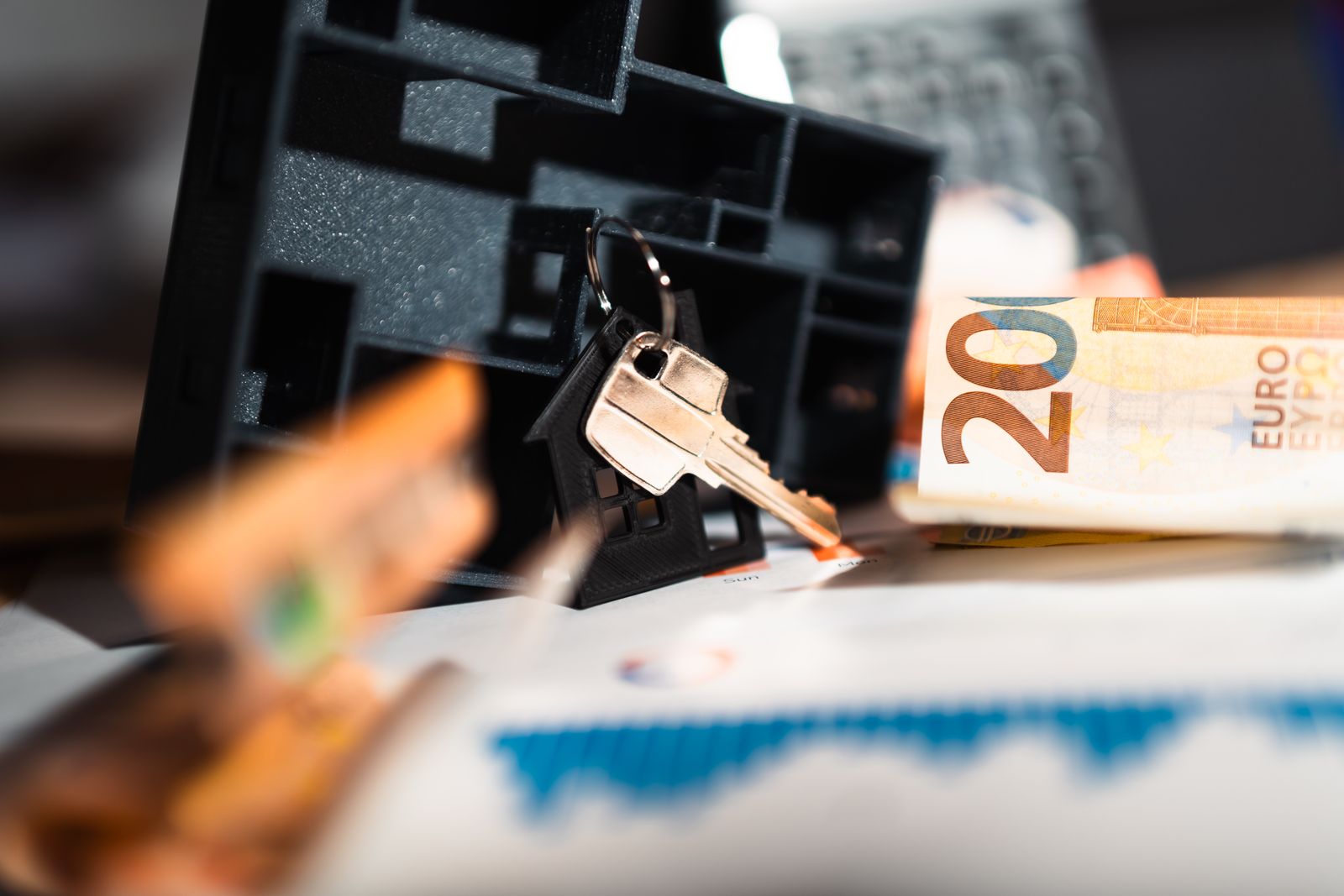 Hausmodell mit Schlüsseln, Euro-Scheinen und Finanzdiagrammen auf Holztisch
