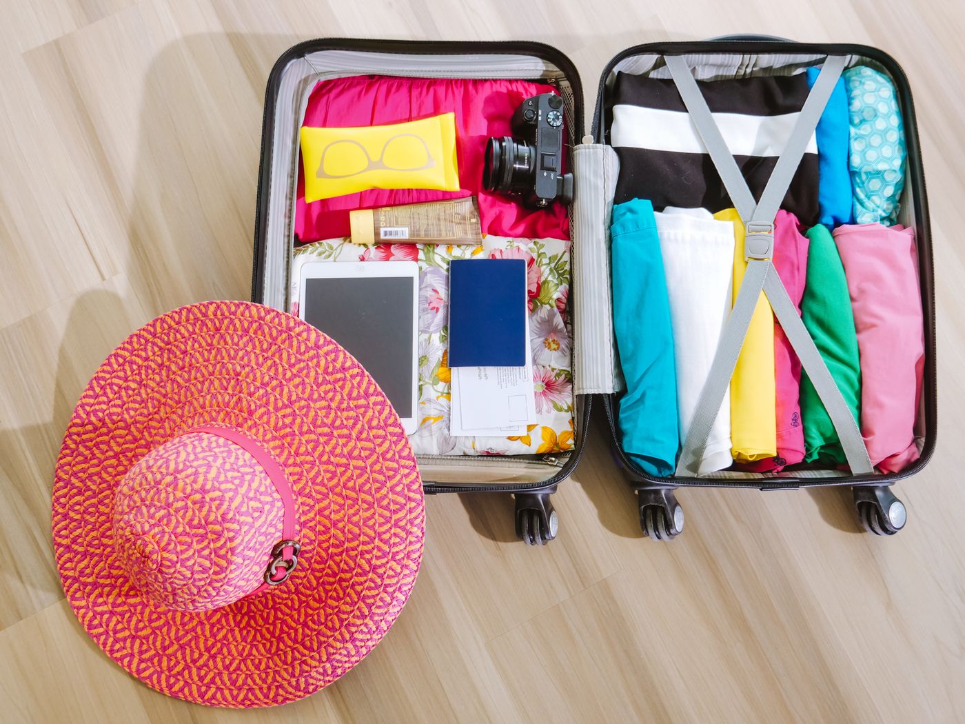 Gepackter Koffer von oben mit gefalteter Kleidung, Sonnenhut und Kamera
