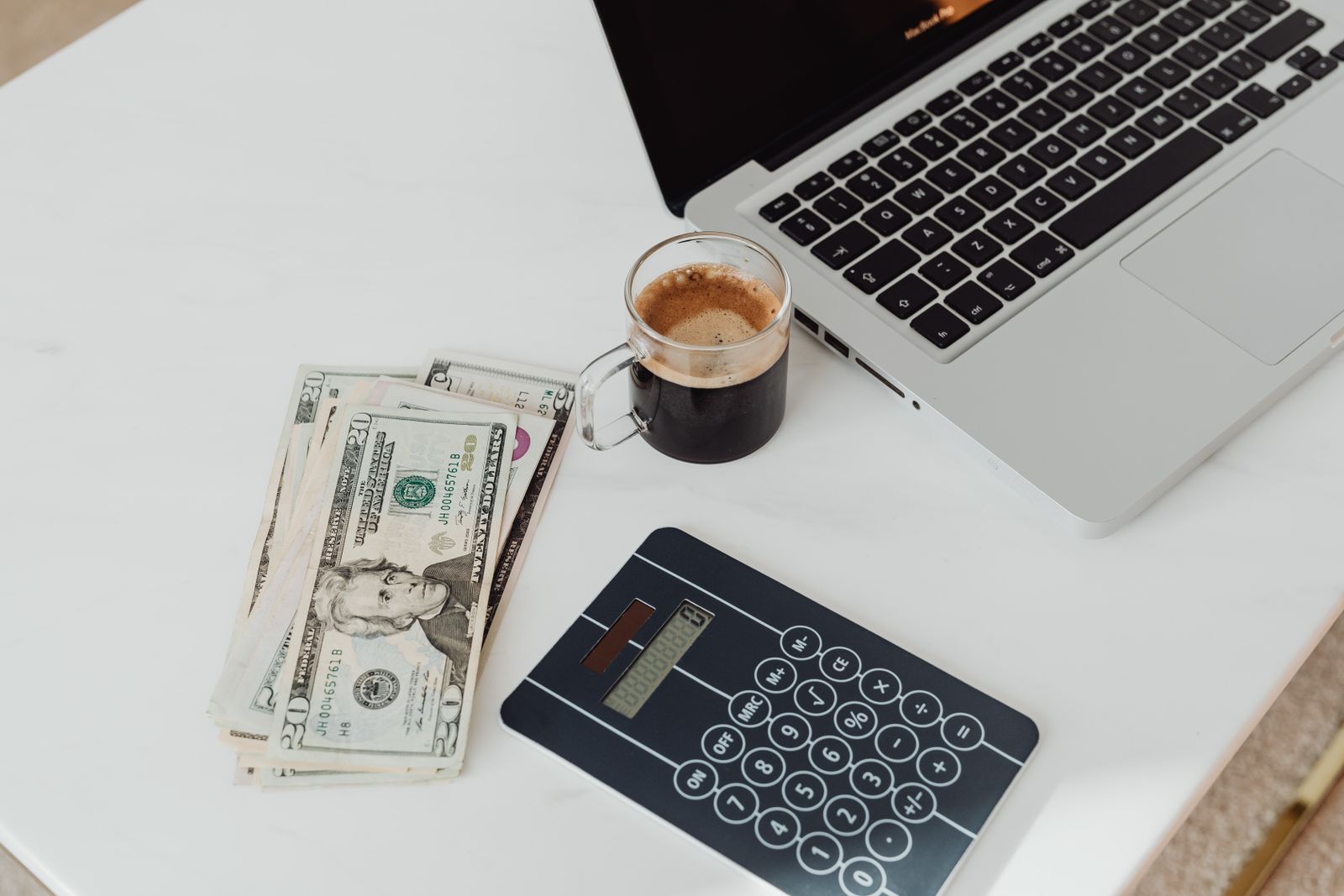 Laptop, Taschenrechner, Bargeld und Kaffee auf einem Schreibtisch im Arbeitsalltag