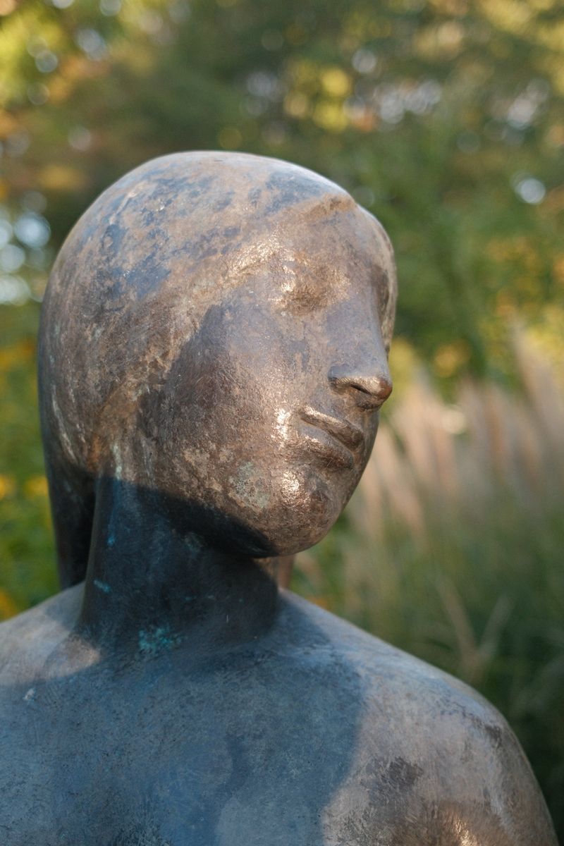 Bronzeskulptur mit graubrauner Patina in einem sonnenbeschienenen Garten