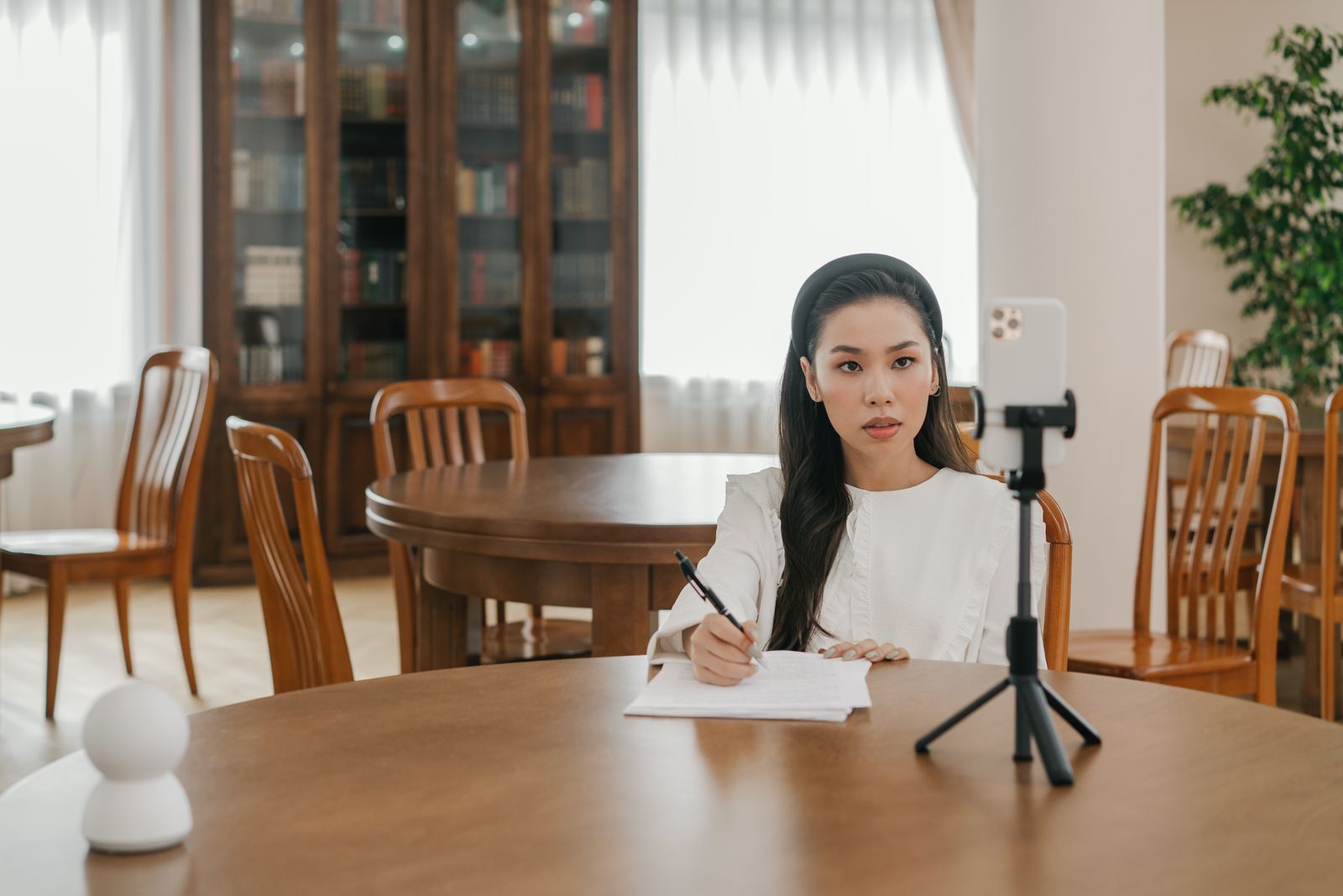Content-Creatorin filmt am Tisch mit Smartphone auf Stativ und Notizen