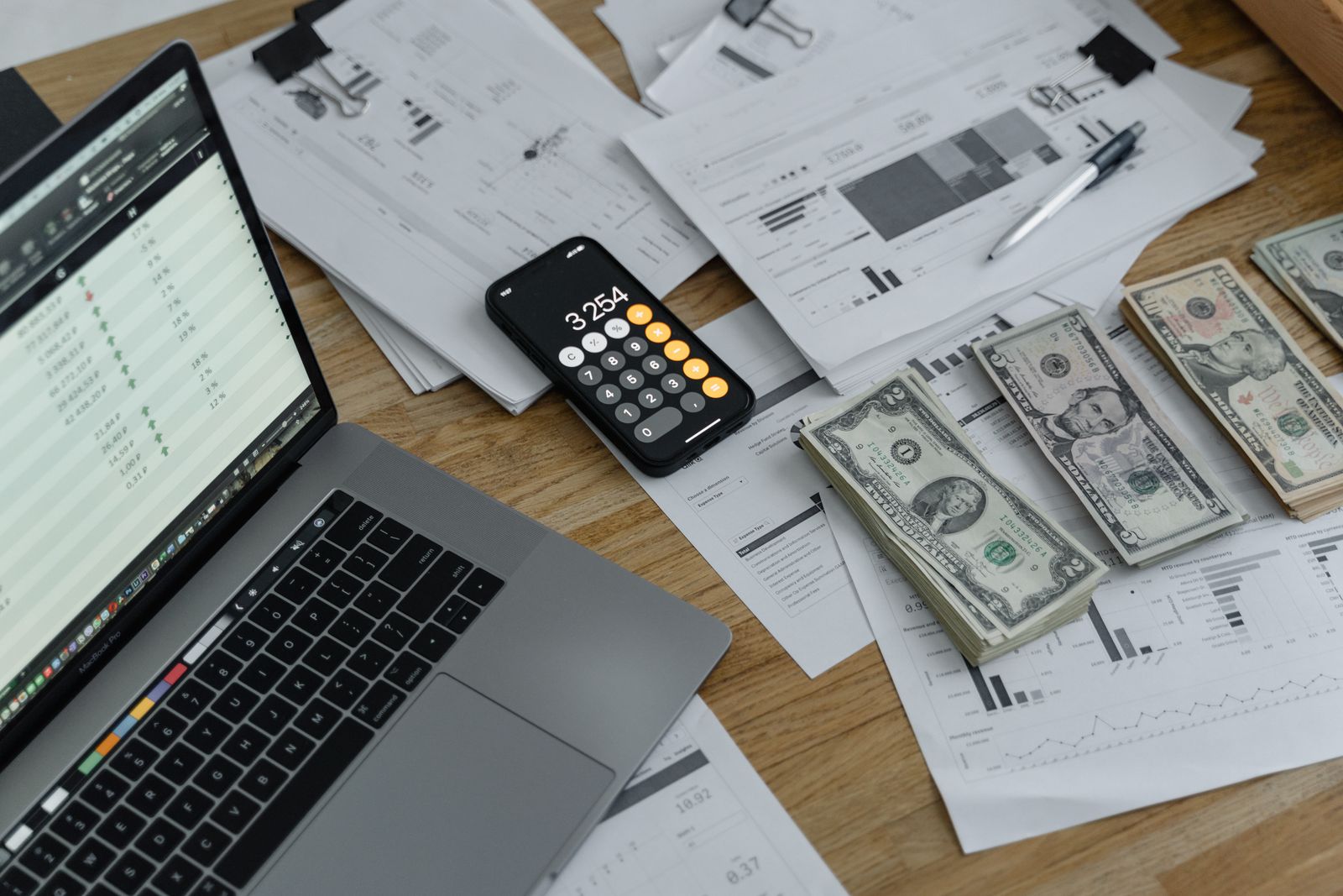 Schreibtisch mit Finanzdokumenten, Bargeld, Laptop und Taschenrechner beim Gehaltscheck