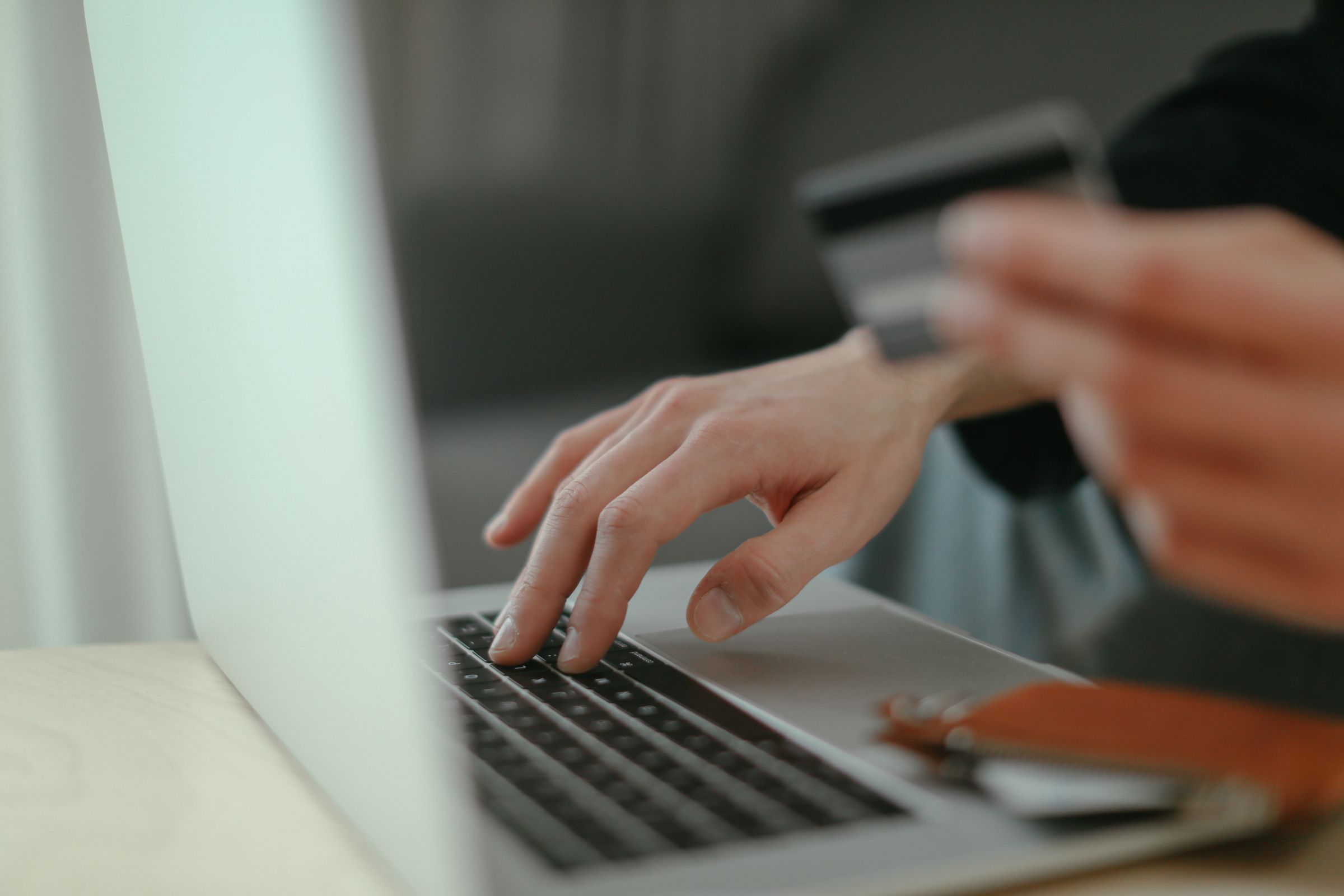 Hand tippt auf Laptop-Tastatur, zweite Hand hält Kreditkarte für einen Online-Einkauf