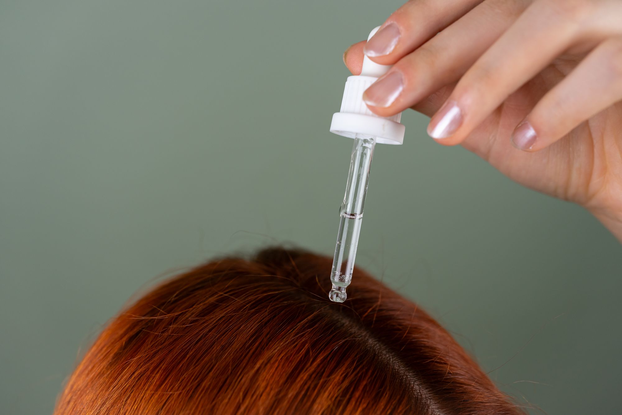 Frau trägt mit einer Pipette Haaröl auf ihre Kopfhaut und Haaransätze auf