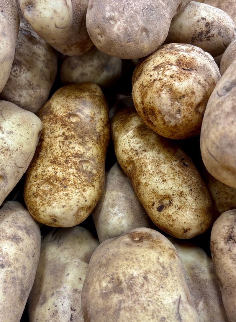 Mehrere rohe Kartoffeln mit Erde in einer Holzschale auf einem Küchentisch