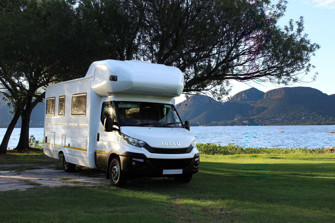Modernes Wohnmobil parkt an einem ruhigen See mit Bergen im Hintergrund
