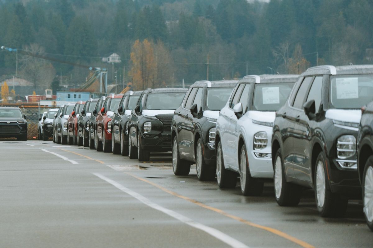 Lange Reihe neuer, dicht nebeneinander geparkter Geländewagen mit Aufklebern an den Seitenscheiben auf einem nassen Asphaltplatz