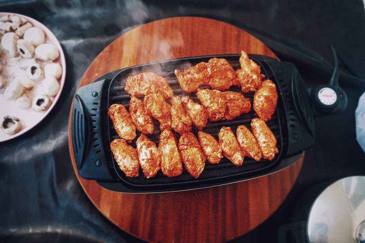 Schwarzer Elektro-Tischgrill mit Temperaturregler und Netzkabel, darauf gegrillte Hähnchenteile