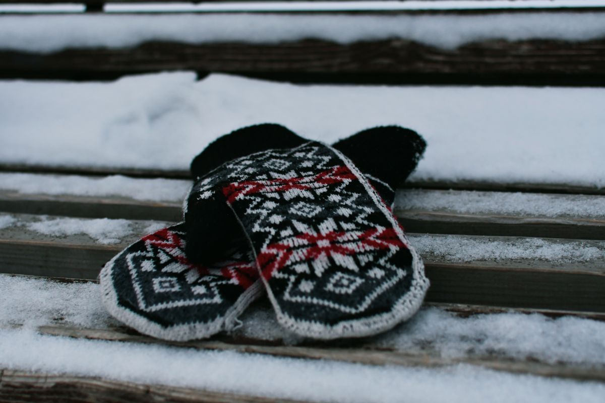 Ein Paar gemusterte Strickfäustlinge liegt auf einer verschneiten Holzbank