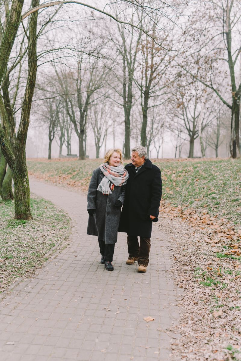 Älteres Paar in Wintermänteln geht einen gepflasterten Weg in einem winterlichen Park entlang